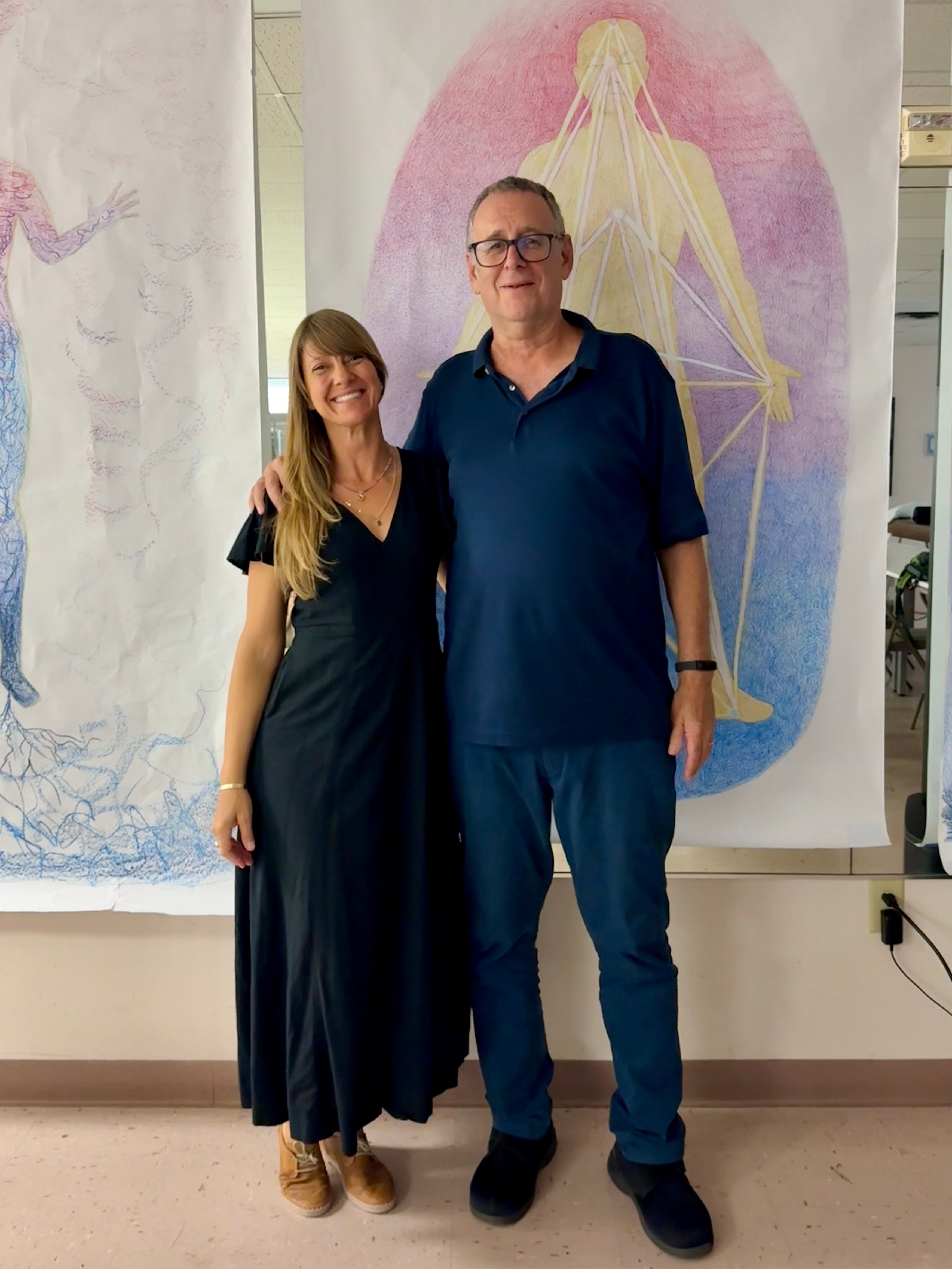Two people standing in front of large abstract artworks on a wall.