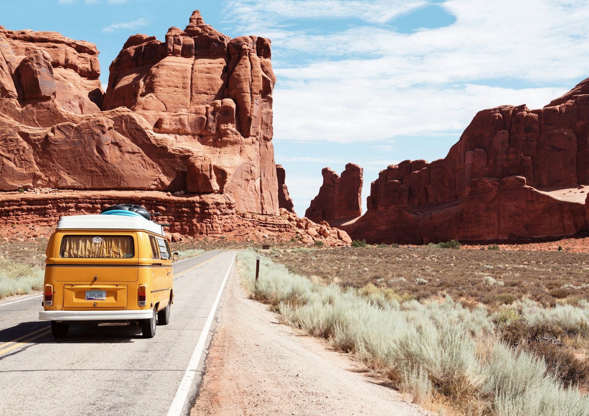 Yellow van on a desert road with red rock formations in the background